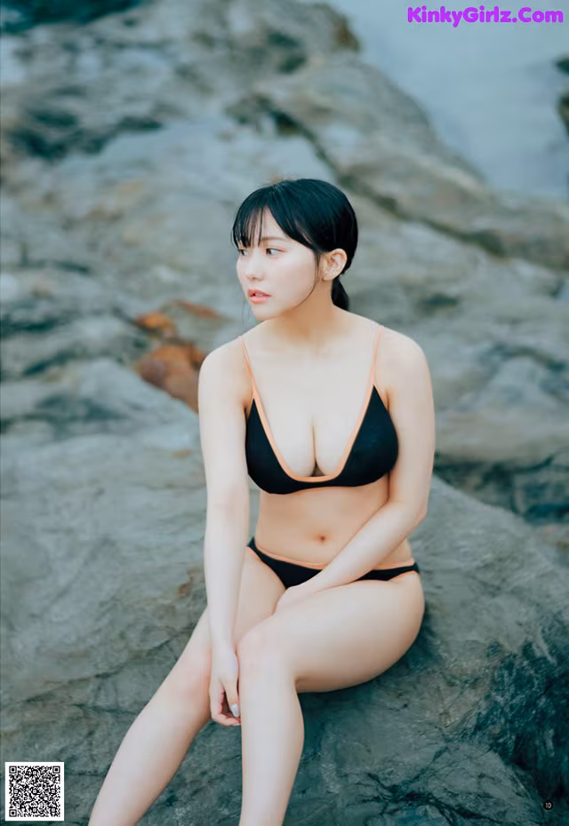 A woman in a black bikini sitting on a rock.