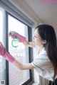 A woman in pink gloves cleaning a window with a spray bottle.