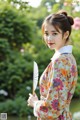 A woman in a floral dress holding a fan.