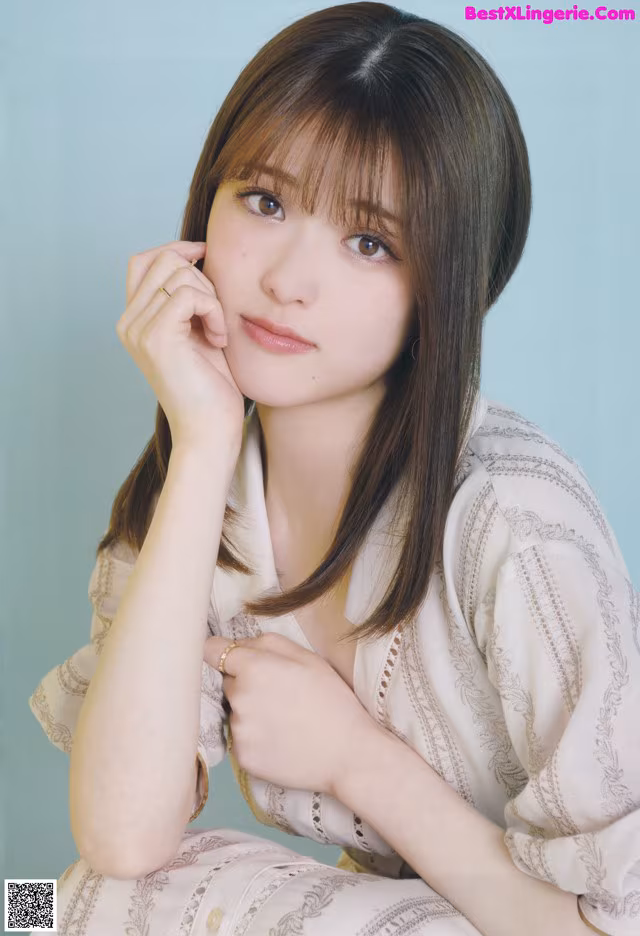 A woman with long brown hair sitting on a blue background.