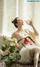 A woman in a white dress sitting next to a vase of flowers.