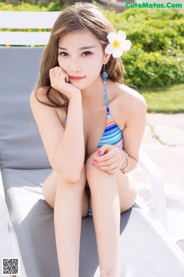 A woman in a bikini sitting on a lounge chair.