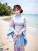 A woman in a blue kimono standing on a beach.