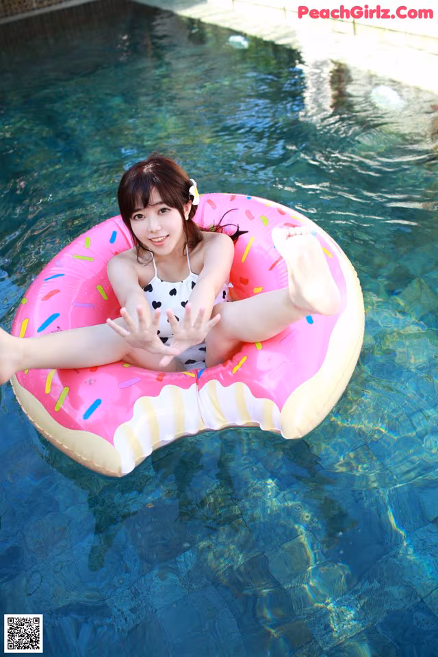 A woman in a bathing suit sitting on an inflatable donut in a pool.