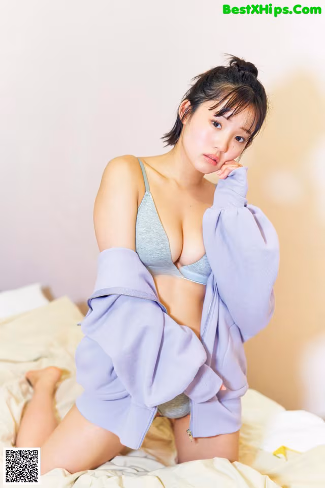 A woman sitting on top of a bed wearing a purple sweatshirt.