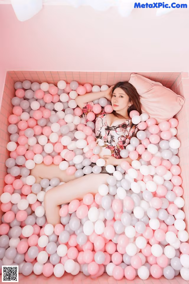 A woman laying in a pink and white ball pit.