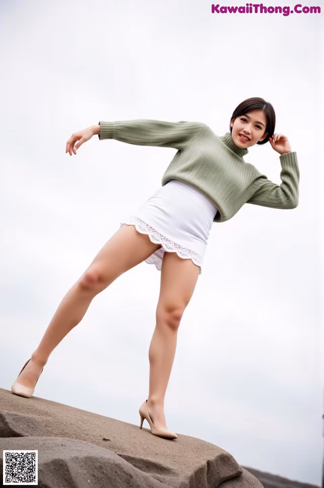 A woman in a green sweater and white skirt posing on a rock.
